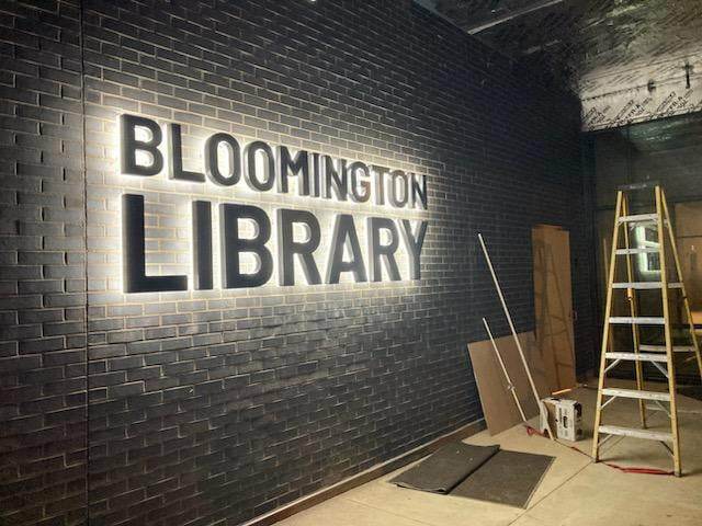 New Bloomington Library sign lit up at night on the Olive Street entrance to the building