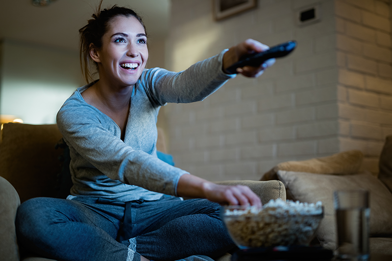 Woman on her couch eating popcorn and watching Blu-Ray