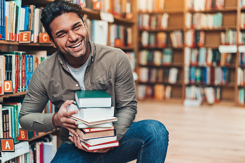Man smiling and holding a stack of books in the library