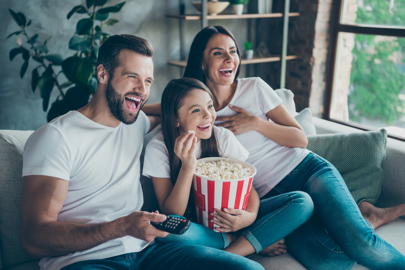Wife, husband and daughter enjoying popcorn and a movie in their living room