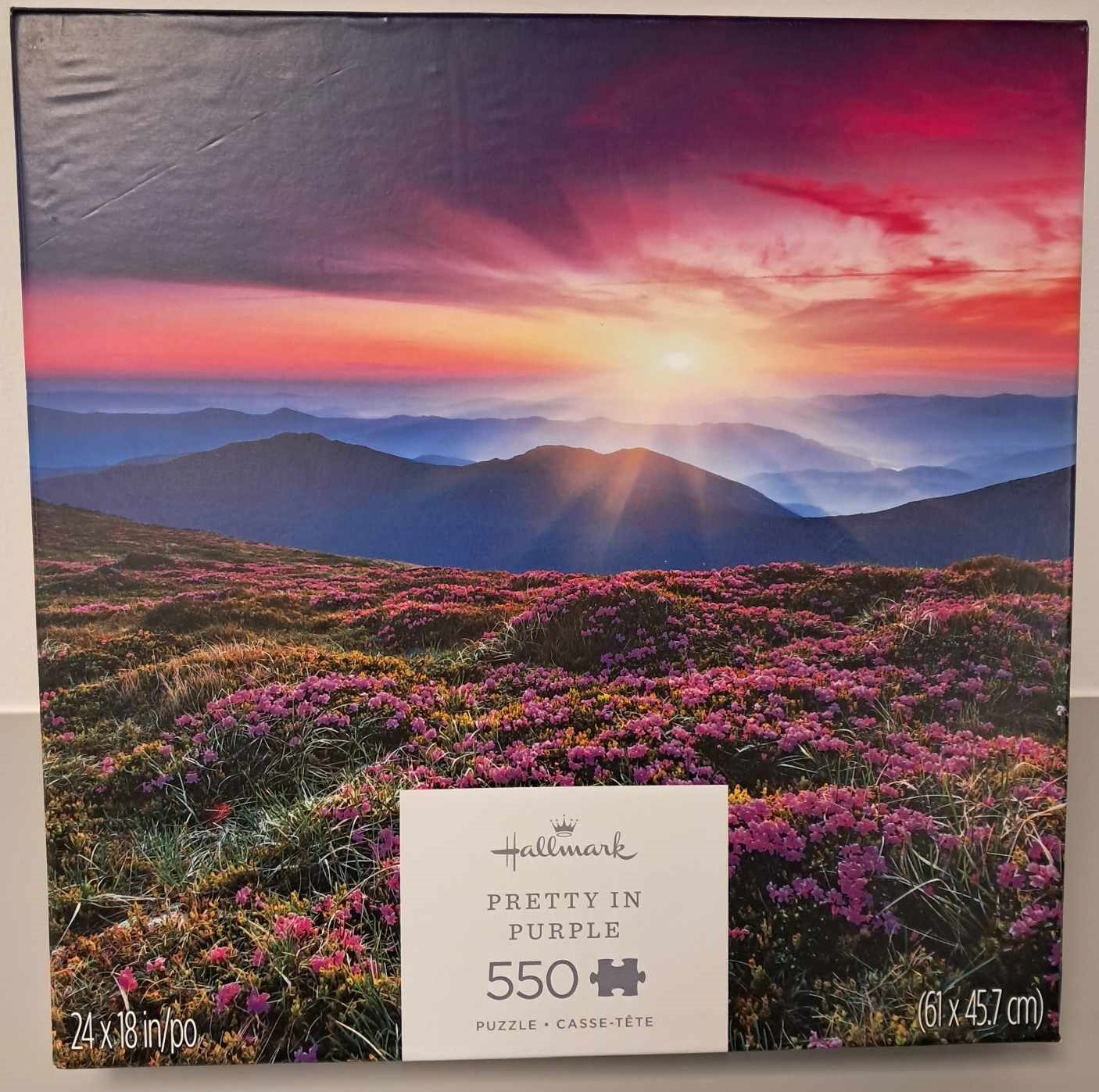 Puzzle cover that shows an image of a sunrise over a mountain range near a field of flowers.