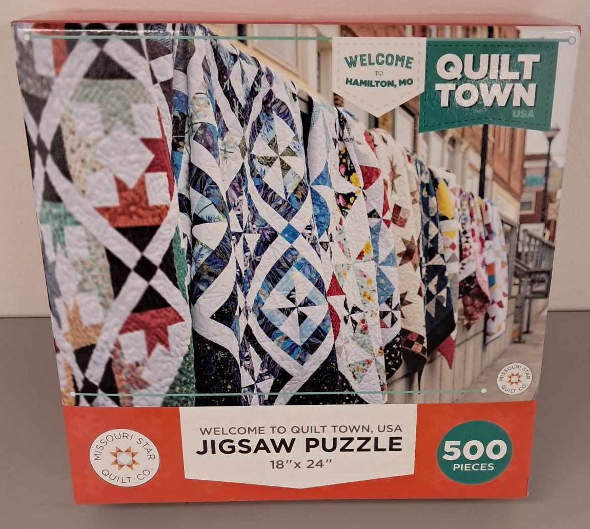Puzzle cover showing a photograph of multiple quilts with different colors and patterns hanging up.