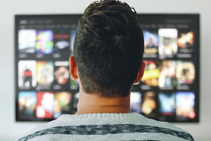 man staring at a TV screen with lots of movie options.