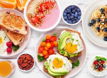 Multiple Dishes of food including fried eggs on avocado toast, oat meal, and different fruits.