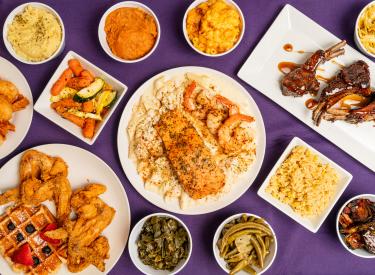 Multiple Dishes of food including shrimp, lamb chops, fried chicken, rice, mac n' cheese, and more.