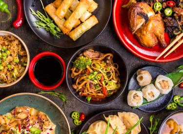 Multiple Dishes of food including dumplings, spring rolls, noodles, chicken, rice and more.